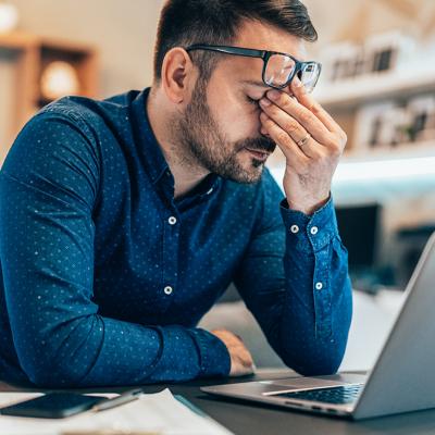 A man rubs his eyes as he sits in front of a laptop.