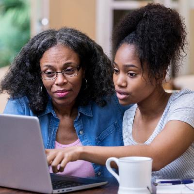 Mother and daughter sitting together while browsing on a laptop. 