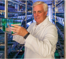Man in white coat surrounded by vials looks at the camera