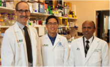 Three men in lab coats smile at the camera