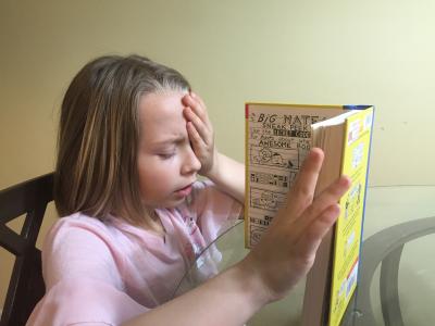 Child reading book with one hand covering an eye