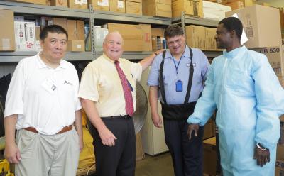 Coworkers stand in front of shelves with boxes.