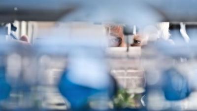 Scientist viewed through a laboratory shelf filled with bottles
