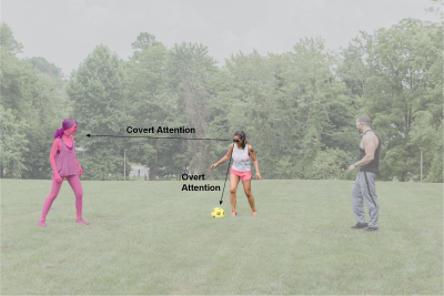 Three soccer players on a field. Center player looks down at the ball by her feet.