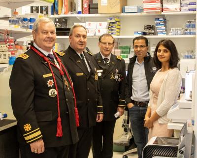 Five people posing an a lab setting - four men and one woman. Three of the men are wearing Knights Templar regalia. 