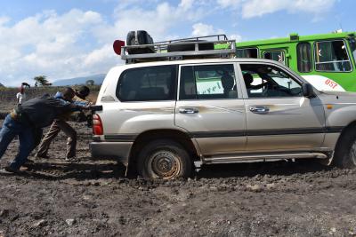 Men push an SUV out of the mud on a sunny day.