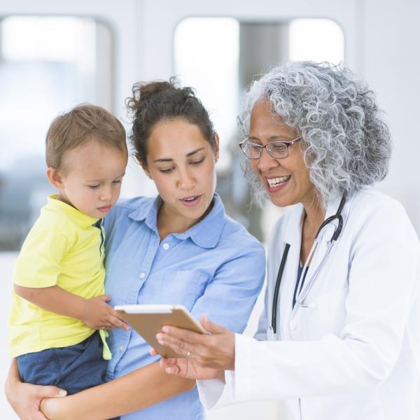 Woman and her young child look at a tablet with their doctor.