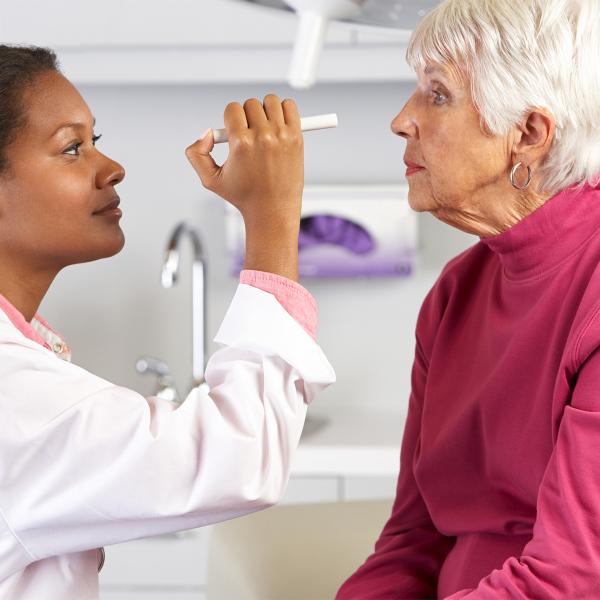 Doctor examining an elderly woman's eyes with a pen light