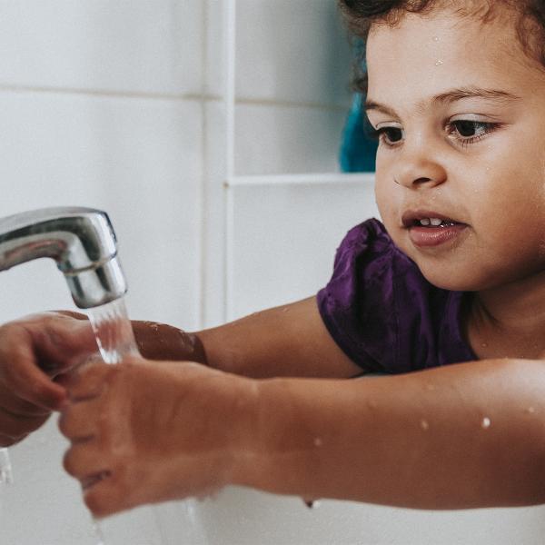 Young child washing their hands in a sink.