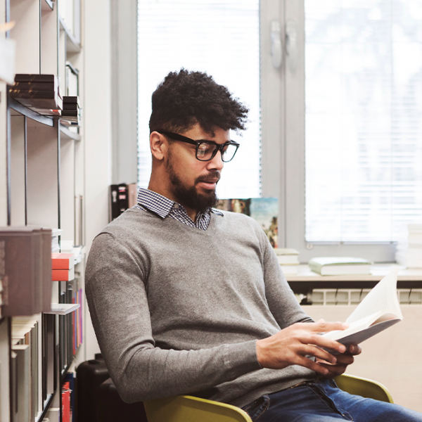 A man who's farsighted wears glasses to read a book he's holding.