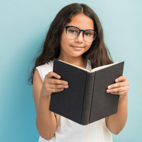 Una niña pequeña usando anteojos, sostiene un libro.