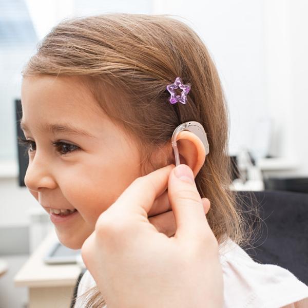 Un profesional de la salud coloca un dispositivo electrónico en la oreja de una niña pequeña para que pueda escuchar mejor.