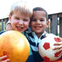2 young boys hold balls and smile at the camera