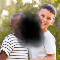 Two young boys smile at camera. A dark spot representing vision loss from AMD blocks the center of the image.